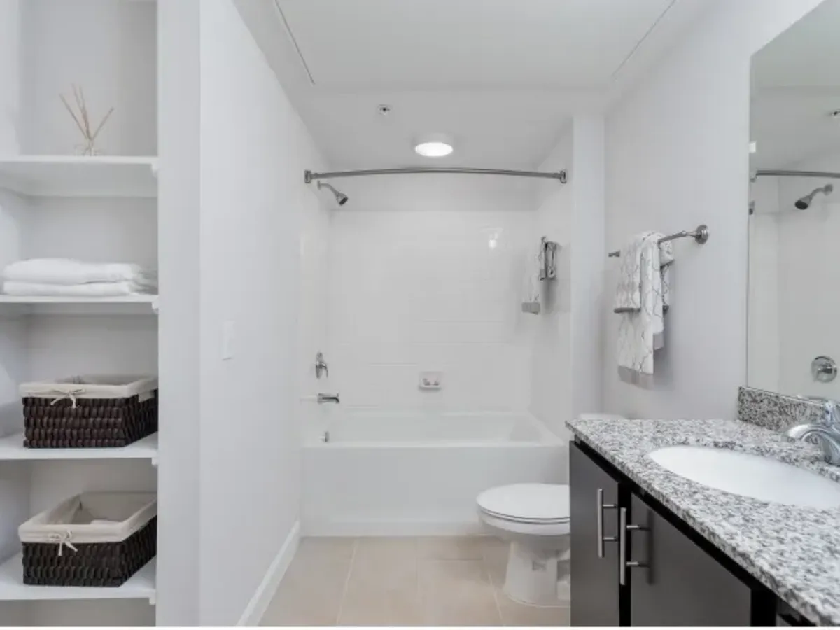 Elegant bathroom featuring a sleek granite countertop, spacious bathtub, and built-in shelving with tasteful storage baskets at The Melrose Apts in Nashville Tennessee.