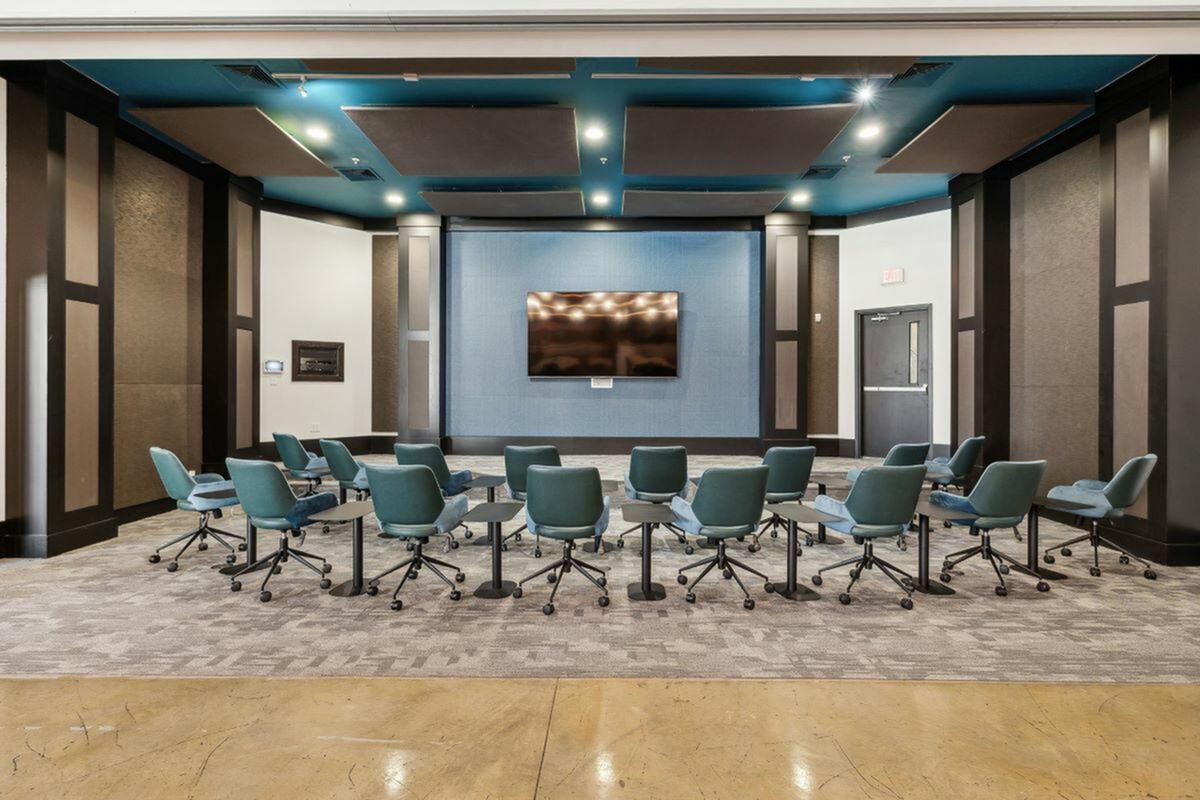 Elegant conference room featuring stylish teal chairs arranged in a semicircle, a large flat-screen display, and sophisticated wall paneling at The Melrose Apartments in Berry Hill, TN.
