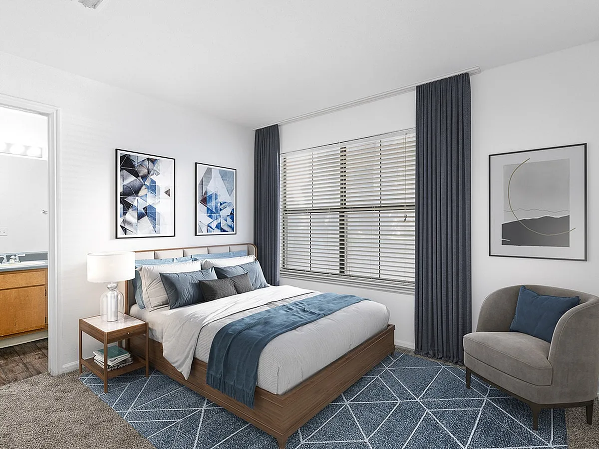Chic bedroom with modern décor, featuring geometric art, plush bedding, and a cozy armchair by a sunlit window at Cottonwood Apartments.