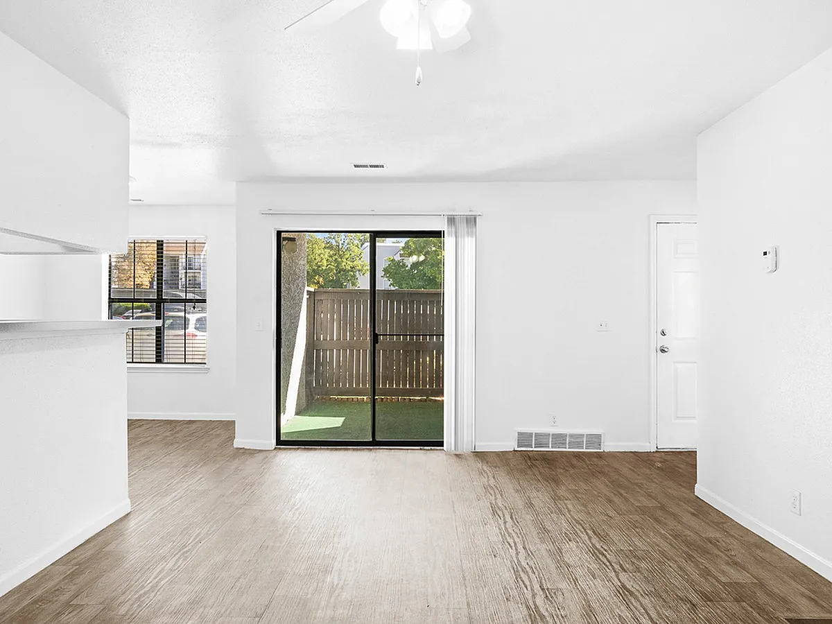 Bright and inviting living area at Cottonwood Apartments with wooden floors and large patio doors opening to a private outdoor space, perfect for relaxation and entertaining.