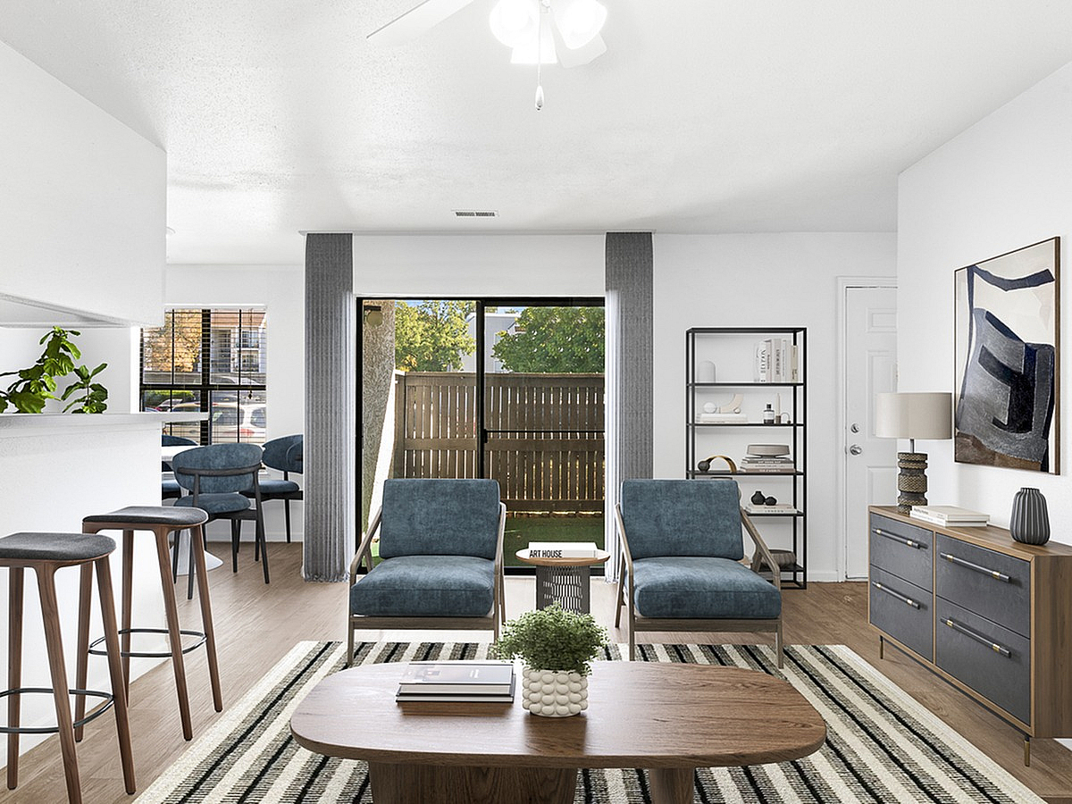 Modern open-concept living area with chic blue chairs, minimalist decor, and natural light from large windows overlooking a private patio at Cottonwood Apartments.