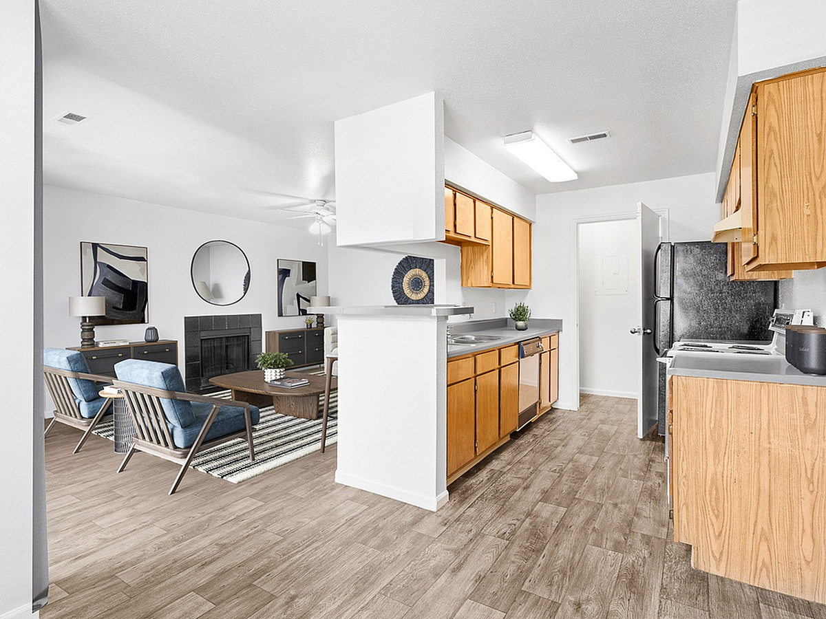 Bright and inviting open-concept living area with modern kitchen, stylish wood cabinetry, and a cozy living room featuring elegant seating and decor at Cottonwood Apartments.