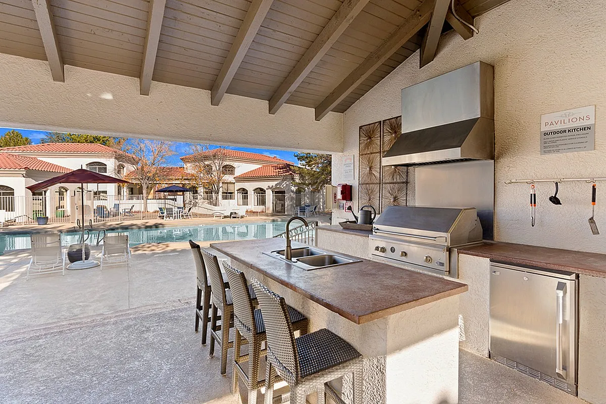 Elegant outdoor kitchen adjacent to a sparkling pool, featuring modern appliances and stylish seating for a luxurious lifestyle at Pavilions Apartments.