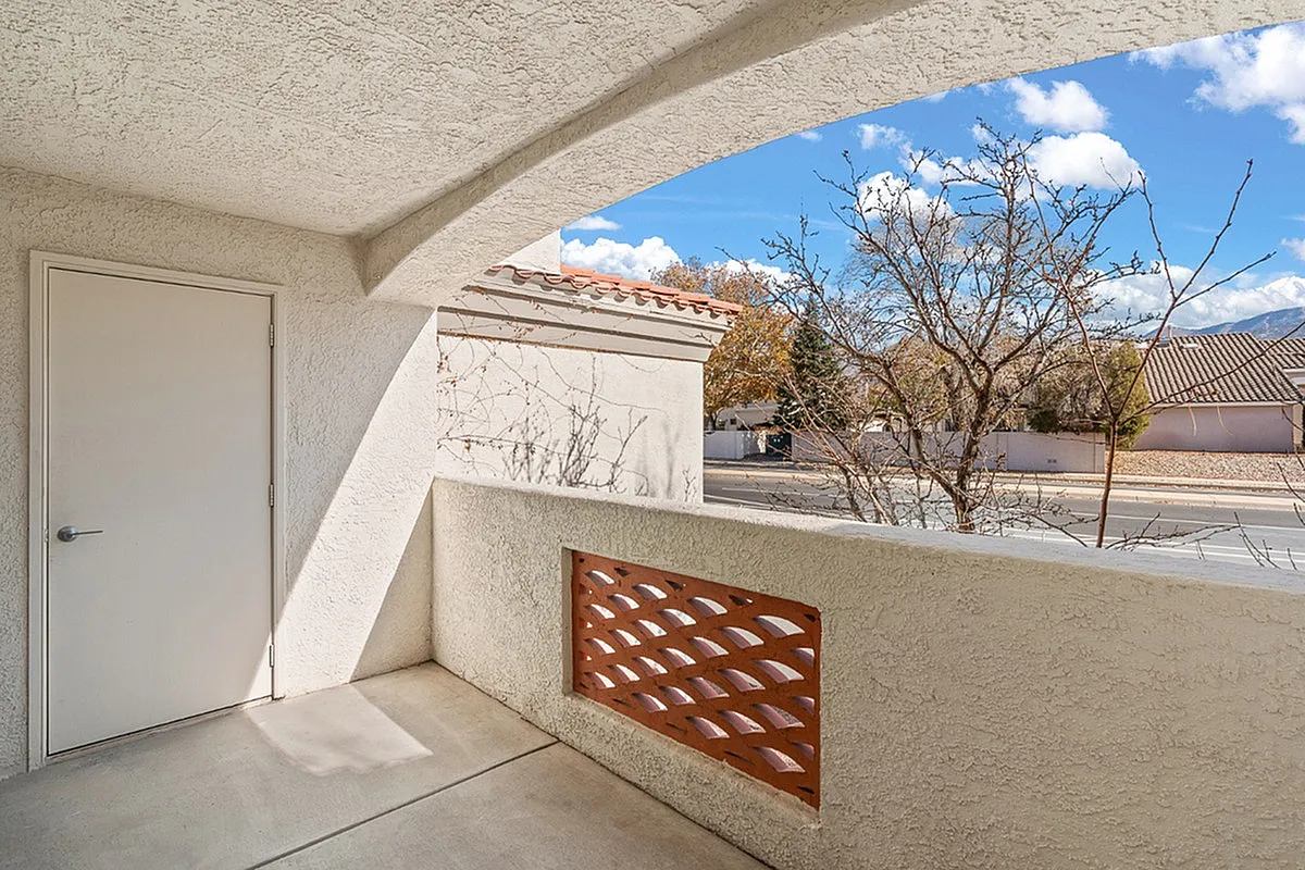 Charming apartment balcony at Pavilions Apartments with stucco walls, offering a sunny view of the neighborhood and clear skies.