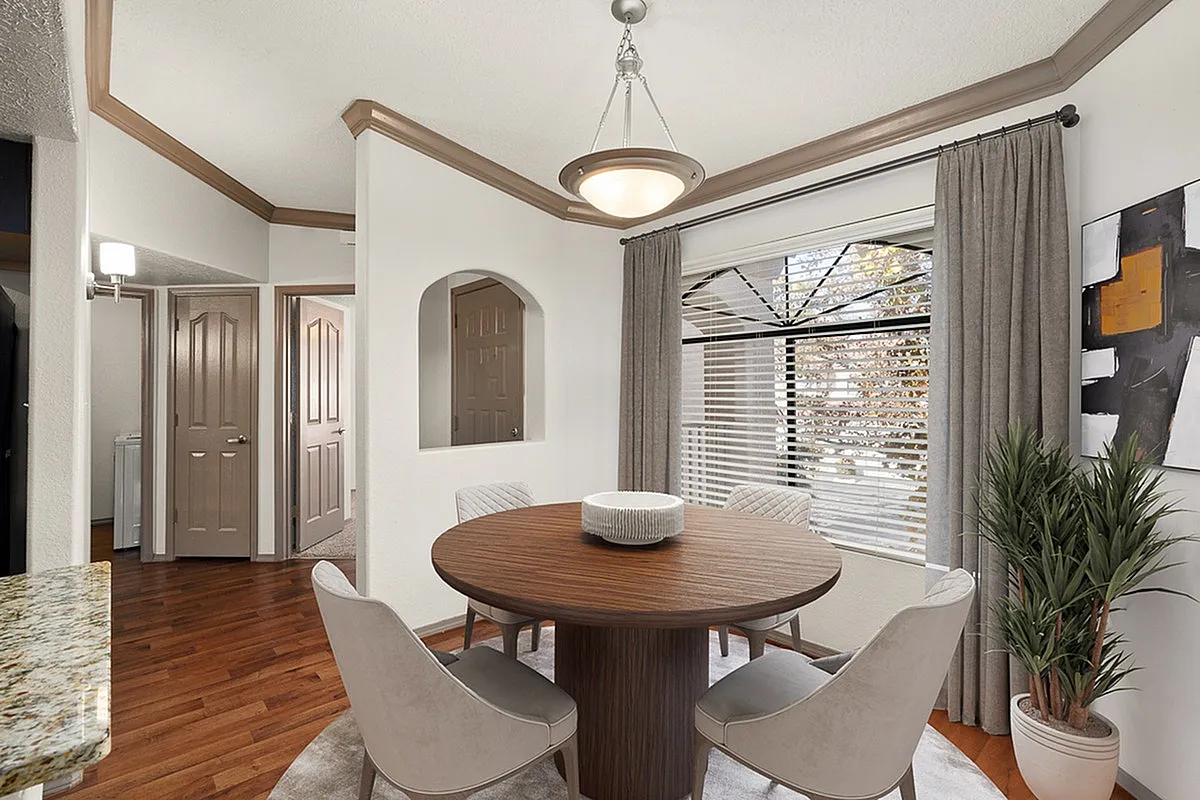 Elegant dining area featuring a round wooden table, plush chairs, and large window with natural light at Pavilions Apartments.