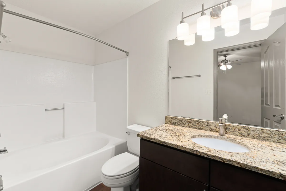 Contemporary bathroom at Pavilions Apartments with elegant granite countertop, built-in bathtub, and stylish lighting fixtures.