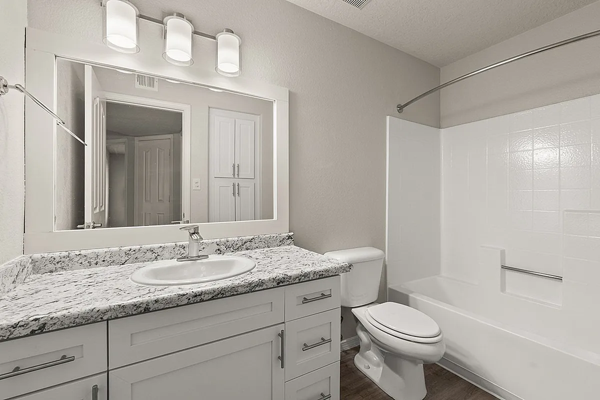 Contemporary bathroom at Pavilions Apartments design featuring sleek granite countertops, bright vanity lighting, and a modern bathtub.