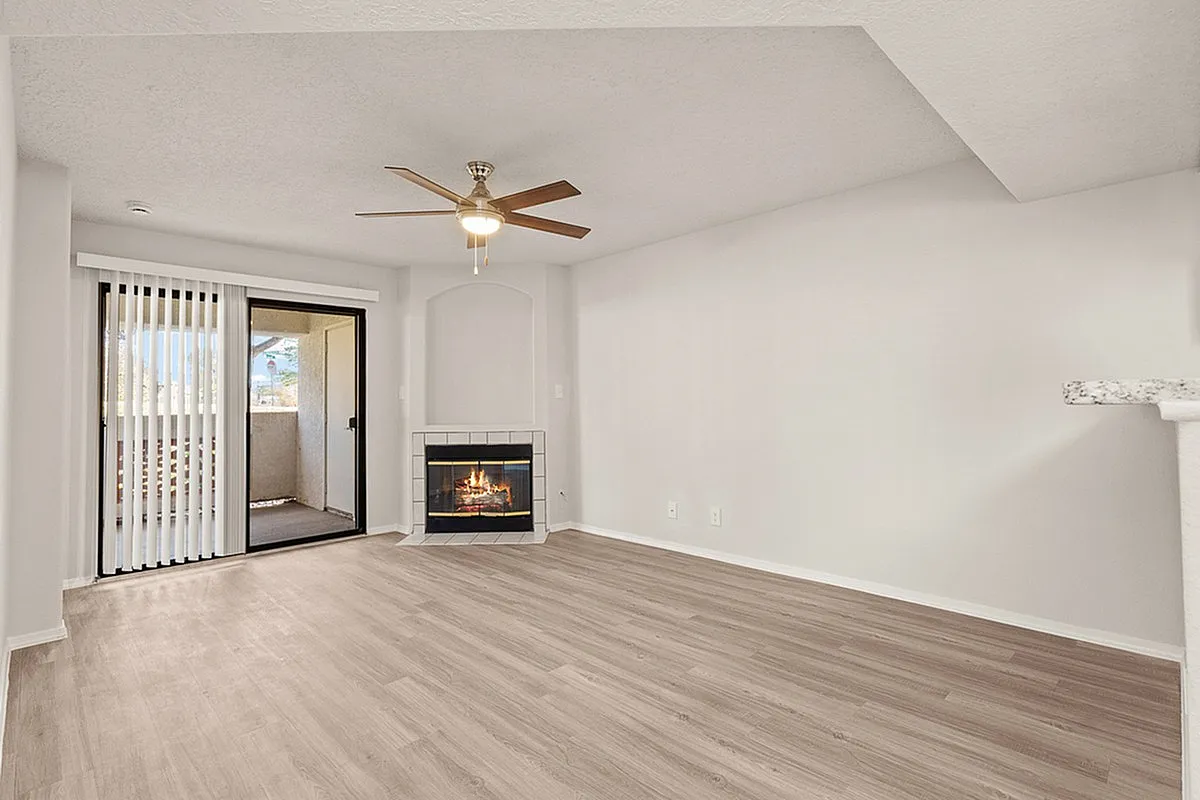 Bright and modern living room at Pavilions Apartments featuring a cozy fireplace, elegant ceiling fan, and sliding glass doors leading to a balcony with scenic views.