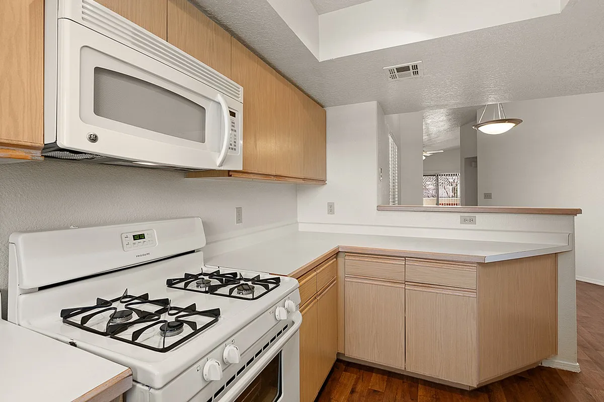 Bright and modern kitchen featuring sleek wooden cabinets, pristine countertops, and essential appliances for a stylish culinary experience at Pavilions Apartments.