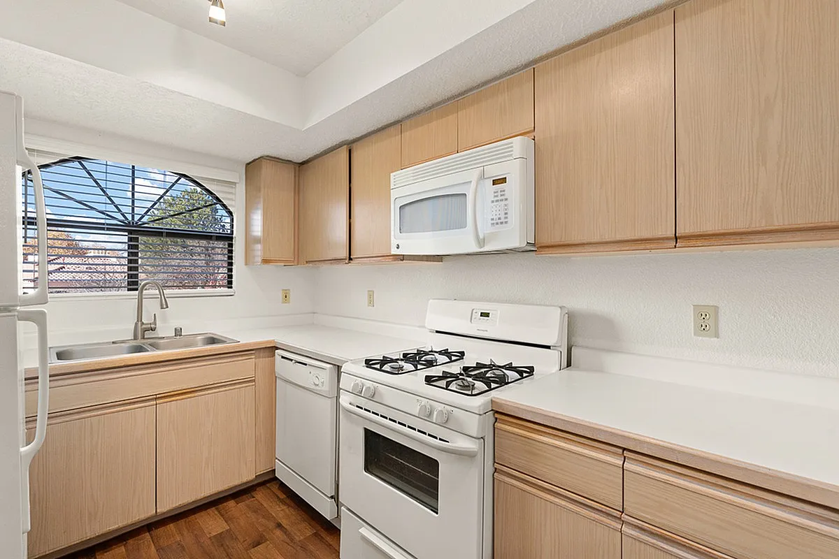 Bright and inviting kitchen with sleek cabinetry, modern appliances, and a charming arched window offering natural light at Pavilions Apartments.