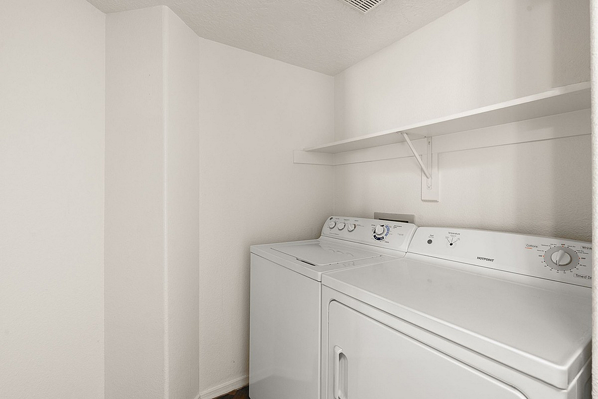 Modern laundry room at Pavilions Apartments with washer and dryer, featuring ample shelving and a crisp, clean design.