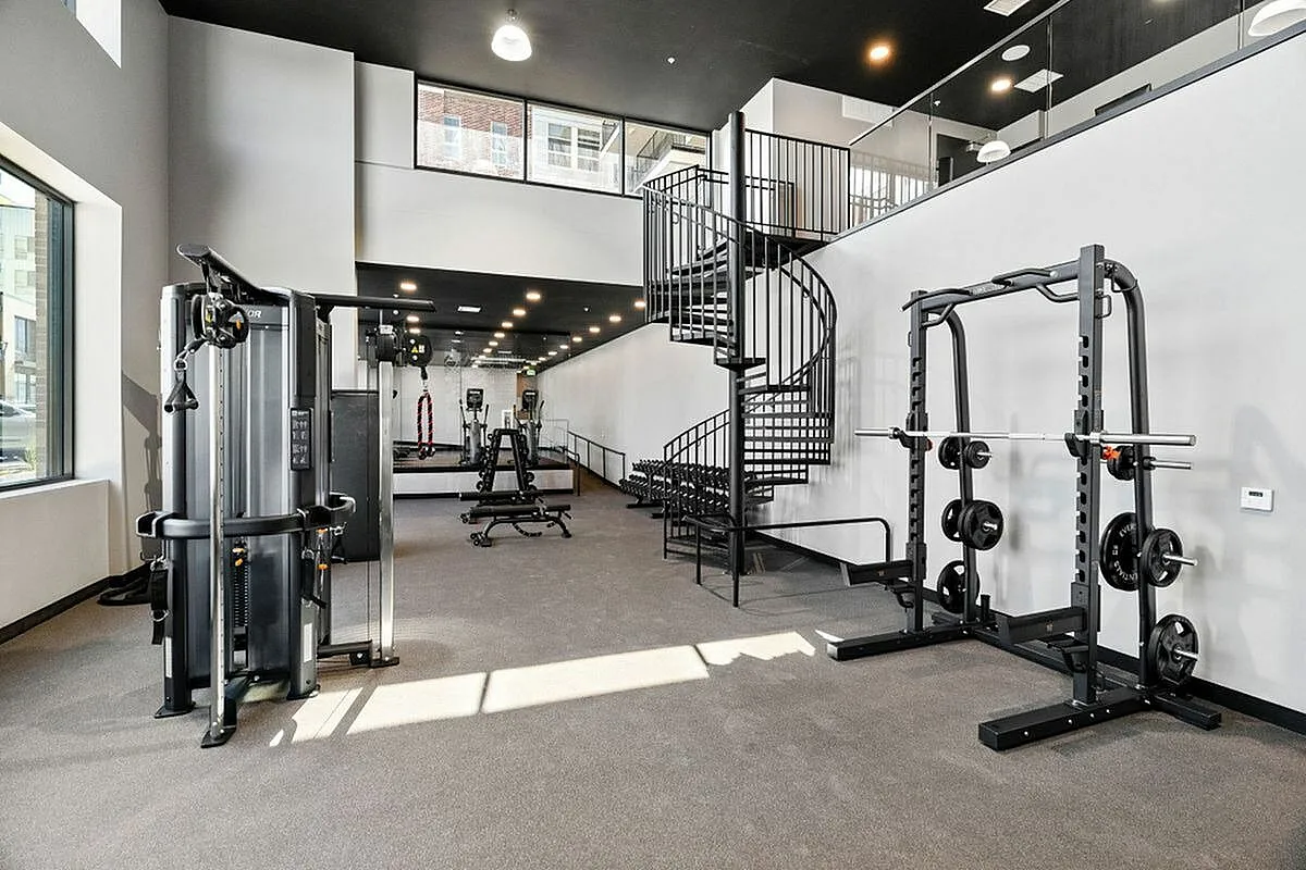 Modern two-story gym space with natural lighting, featuring state-of-the-art fitness equipment and a stylish spiral staircase at The Richmond Apartments in SLC Utah