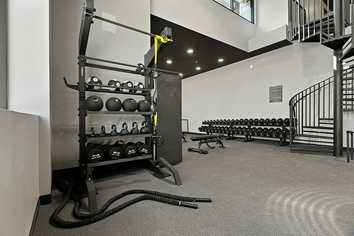 Modern two story fitness center with diverse workout equipment including weights, kettlebells, and battle ropes, featuring stylish spiral staircase and sleek design at The Richmond Apartments in Millcreek Utah