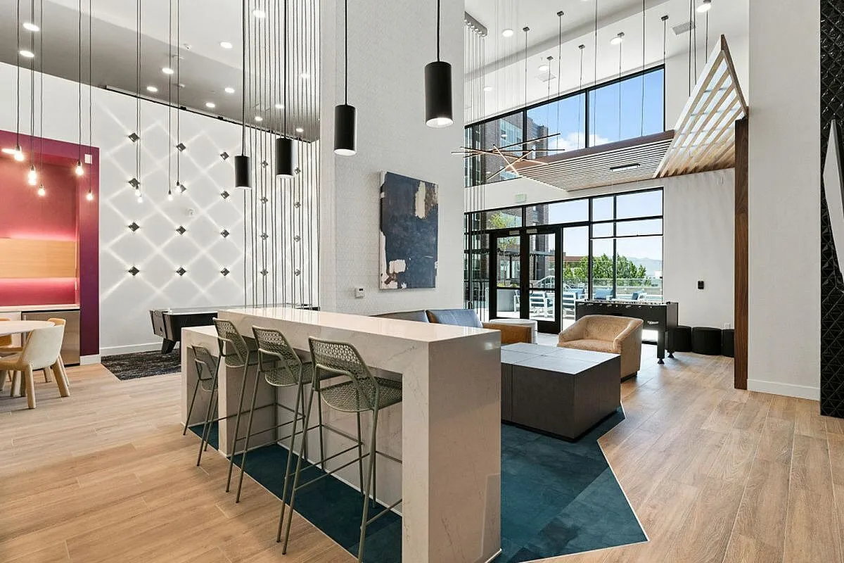Modern apartment clubroom with high ceilings, stylish pendant lighting, and large windows showcasing a bright, inviting space. Features a sleek bar area with chic seating and contemporary artwork  at The Richmond Apartments in SLC Utah