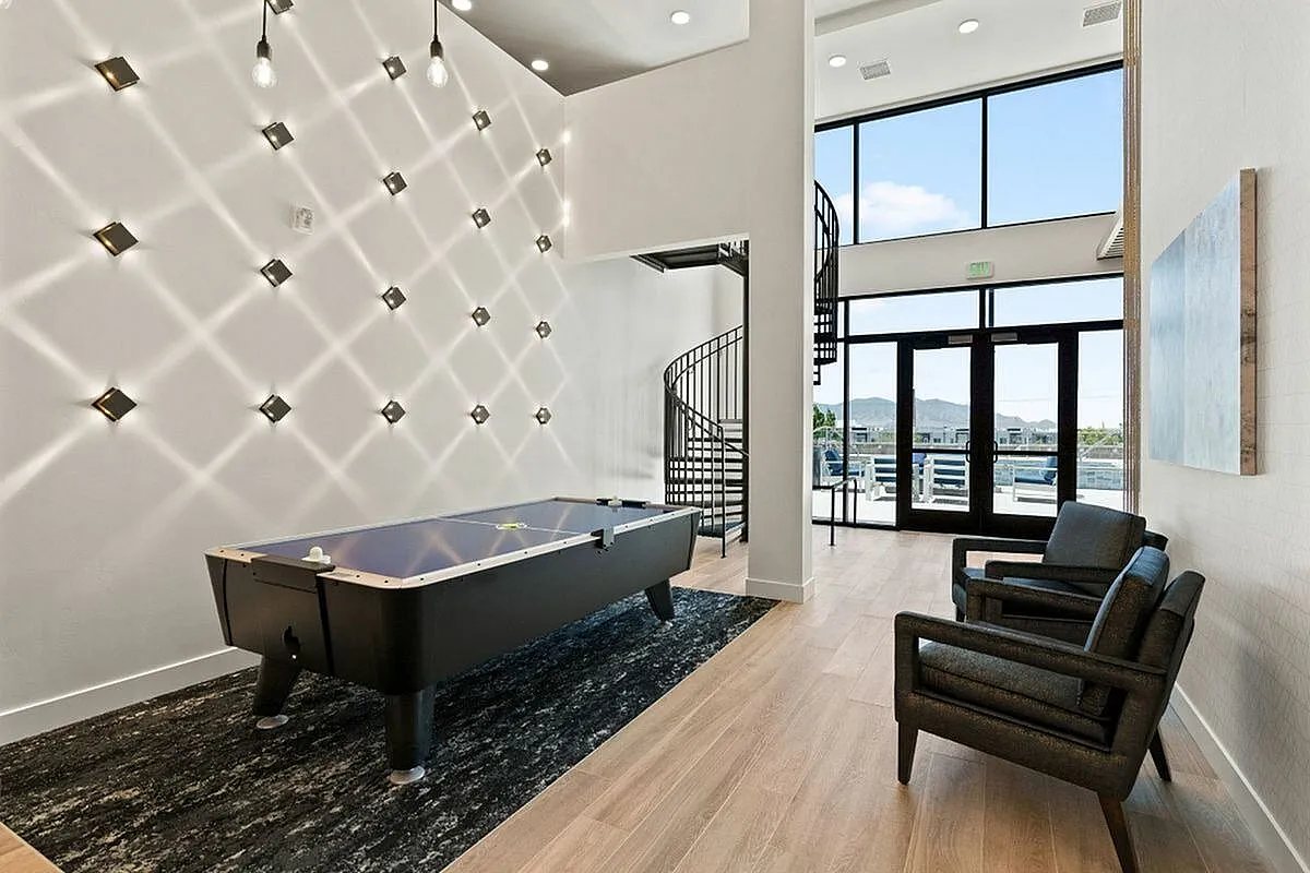 Modern recreational room with stylish lighting, featuring a sleek air hockey table and elegant spiral staircase leading to a balcony with scenic views at The Richmond Apartments in Millcreek Utah