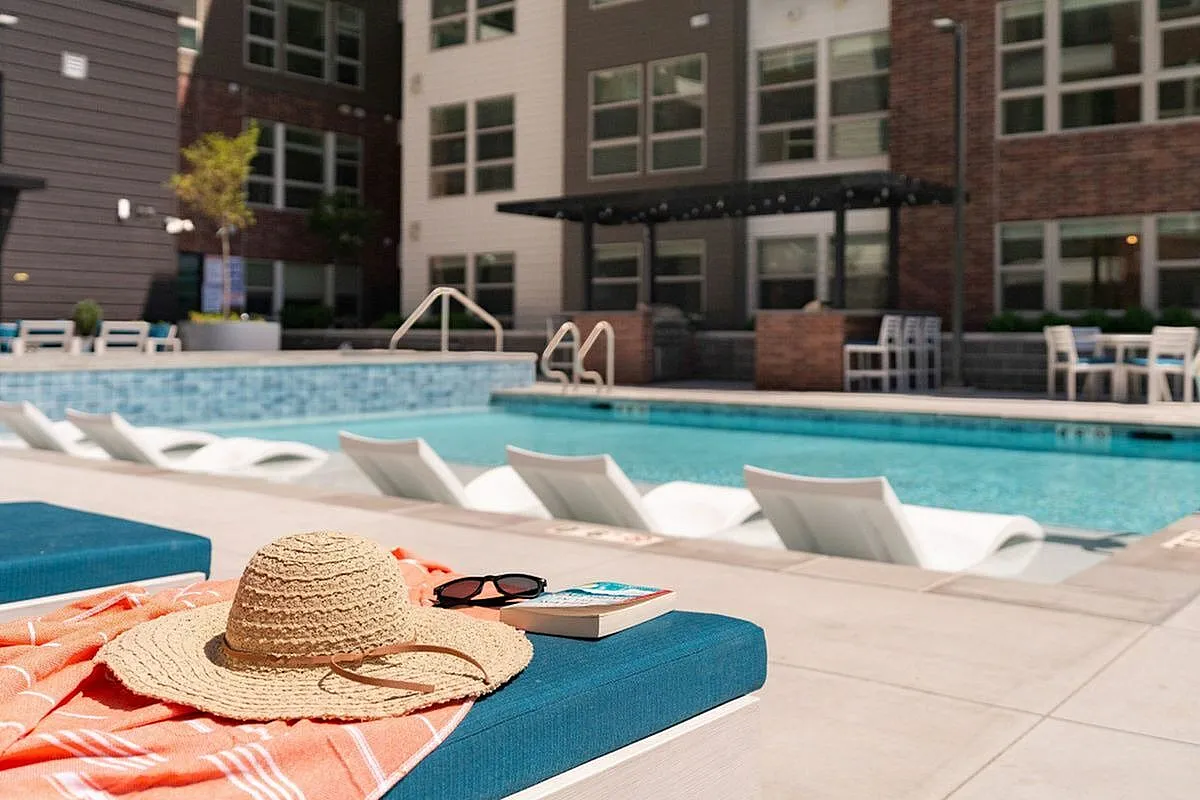 Inviting poolside scene at a modern apartment complex with resort-style lounge chairs, a straw hat, and sunglasses hinting at relaxation and leisure at The Richmond Apartments in Millcreek Utah