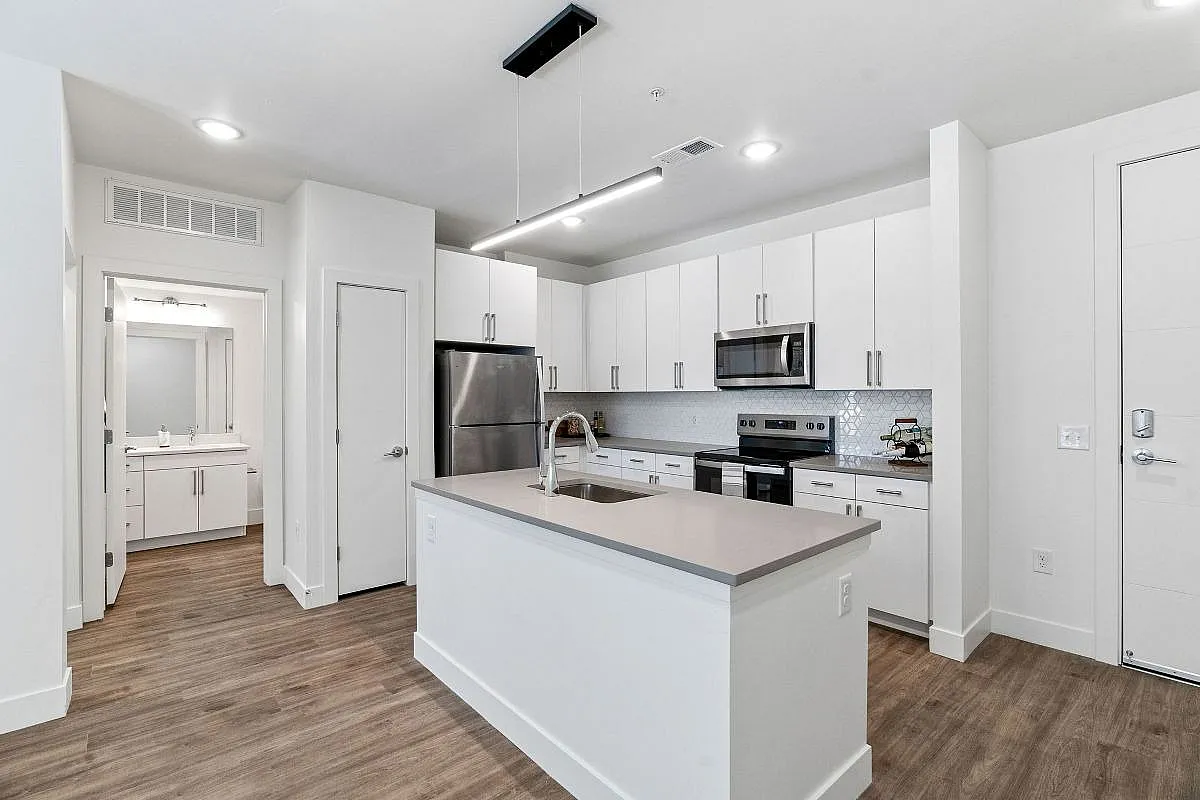 Modern kitchen with sleek white cabinetry, stainless steel appliances, and a chic island in a bright open space at The Richmond Apartments in Millcreek.