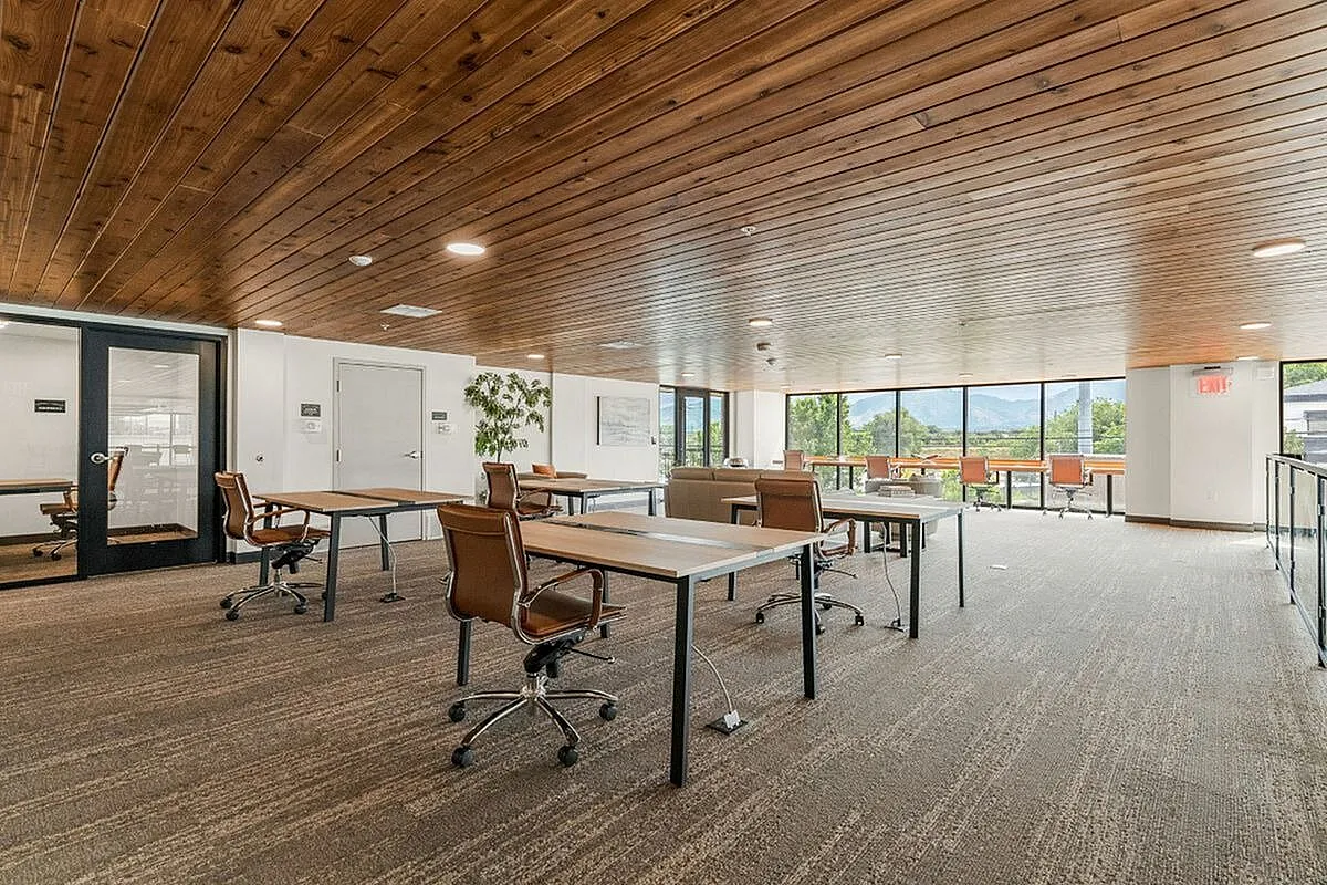 Spacious modern workspace with elegant wooden ceiling, large windows offering vibrant views, and sleek brown chairs for a productive environment  at Current Apartments in Salt Lake City Utah