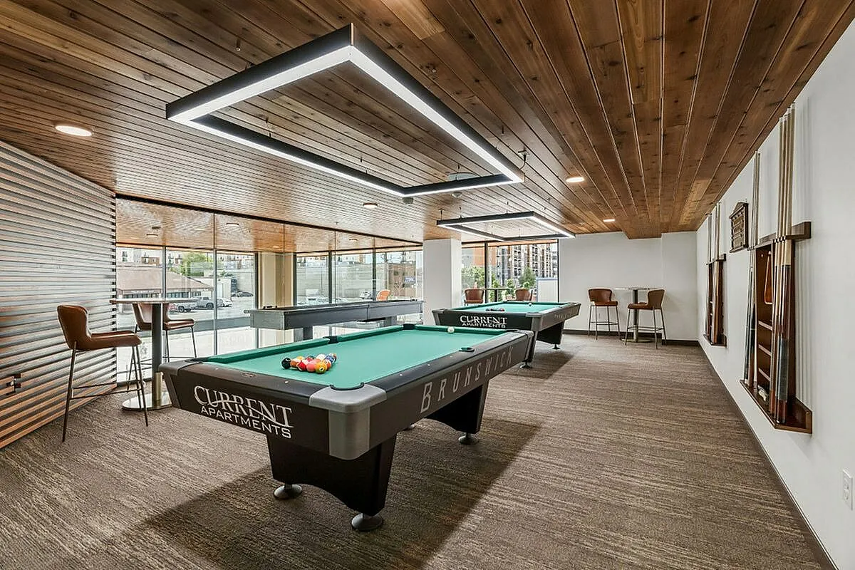 Chic apartment game room featuring modern billiards tables, stylish seating, and expansive city views through large windows  at Current Apartments in Murray Utah