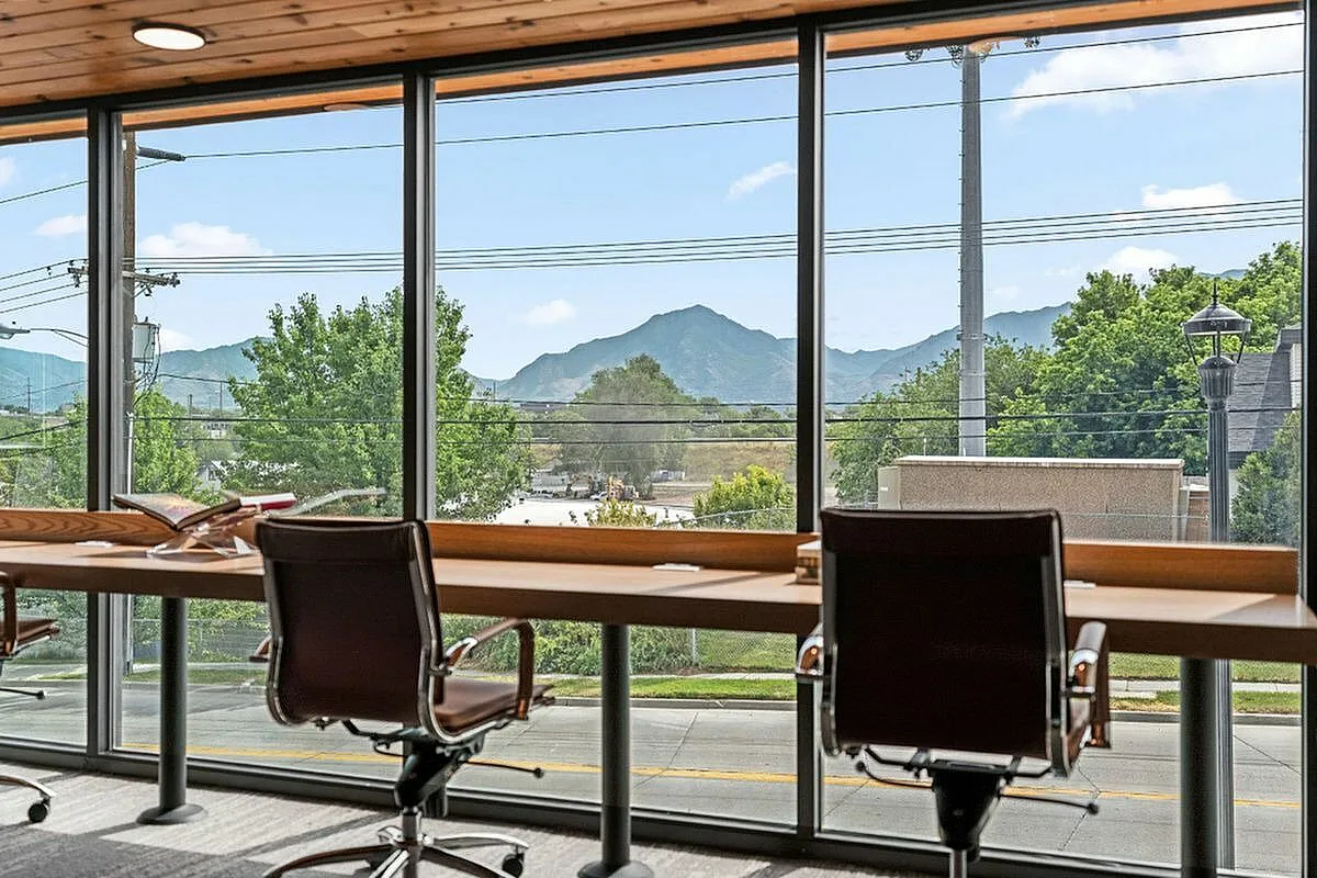 Modern office space with large windows offering breathtaking mountain views, featuring sleek chairs and a stylish wooden desk  at Current Apartments in Murray Utah