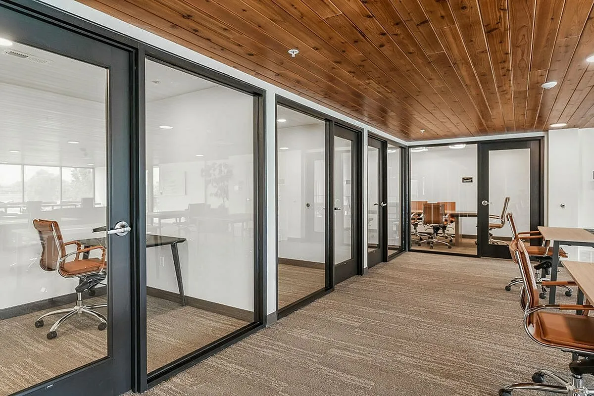 Modern office space featuring sleek glass doors, stylish wooden ceiling, and comfortable leather chairs in a collaborative workspace  at Current Apartments in Murray Utah