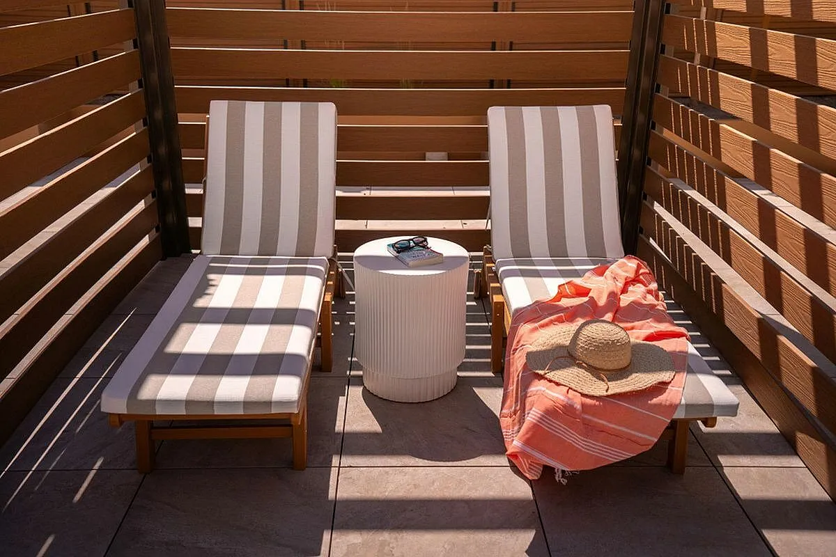 Inviting outdoor patio with two striped chaise lounges, a side table, and a sun hat basking in warm sunlight  at Current Apartments in Murray Utah