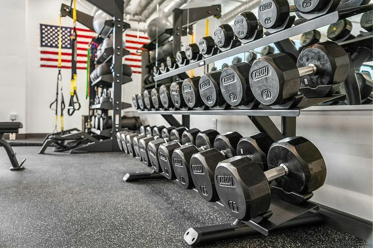 Modern fitness center featuring a variety of free weights organized neatly on racks, with an American flag adorning the background  at Current Apartments in SLC Utah