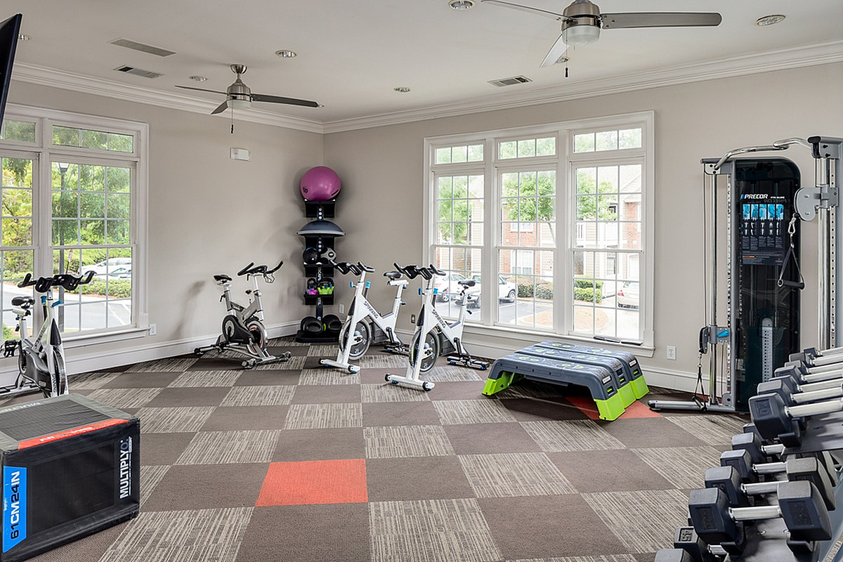 Contemporary gym at Retreat at Peachtree City Apartments with exercise bikes, weights, and modern equipment set in a bright room with large windows.