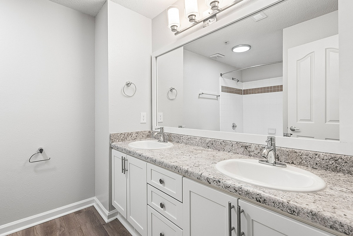 Chic bathroom at Retreat at Peachtree City Apartments featuring a spacious double vanity with elegant granite countertops, polished chrome fixtures, and modern lighting, offering a touch of luxury.
