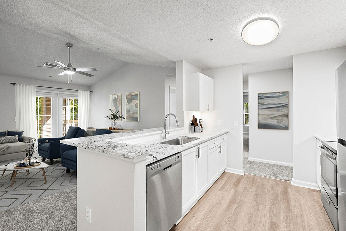 Bright and modern open-concept apartment at Retreat at Peachtree City Apartments kitchen with granite countertops, stainless steel appliances, and elegant living area in the background.