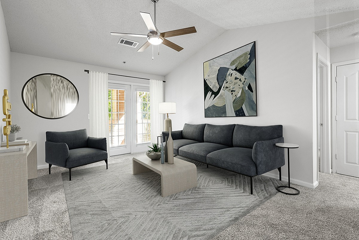 Modern living room at Retreat at Peachtree City Apartments with elegant gray sofa, chic armchair, abstract artwork, and stylish decor on soft gray carpet.