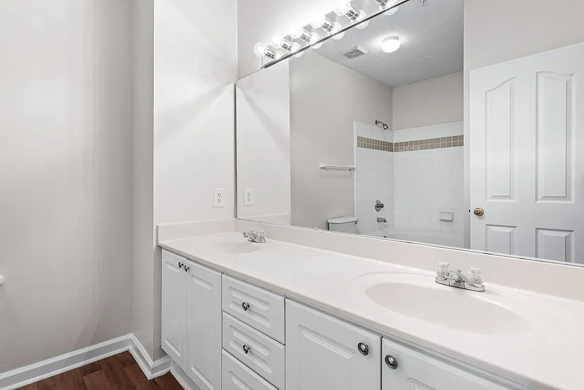 Elegant bathroom at Retreat at Peachtree City Apartments showcasing a dual-sink vanity, large mirror, and a modern bathtub with stylish tiling.