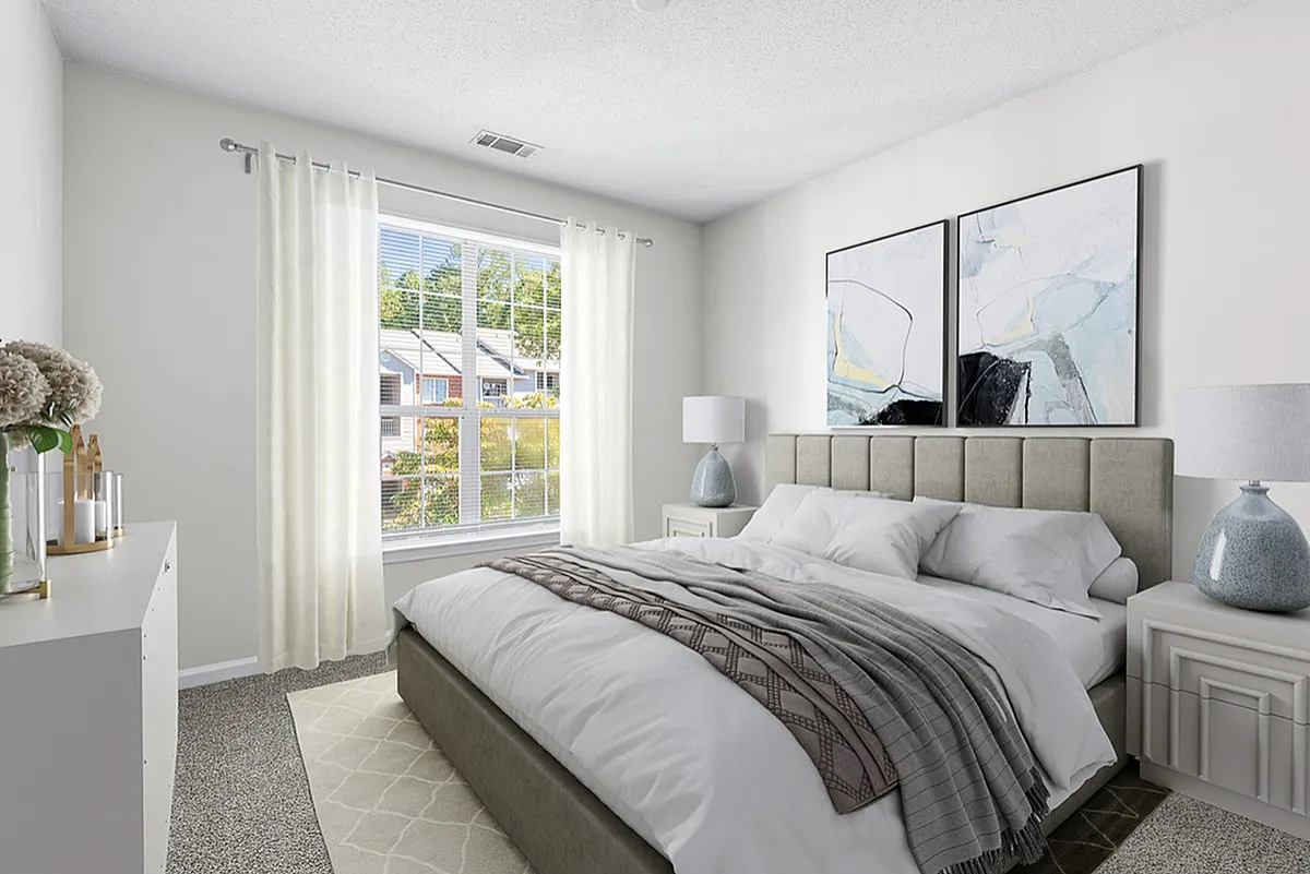 Inviting bedroom at Retreat at Peachtree City Apartments with abundant natural light, featuring a plush bed, stylish artwork, and calming neutral tones.