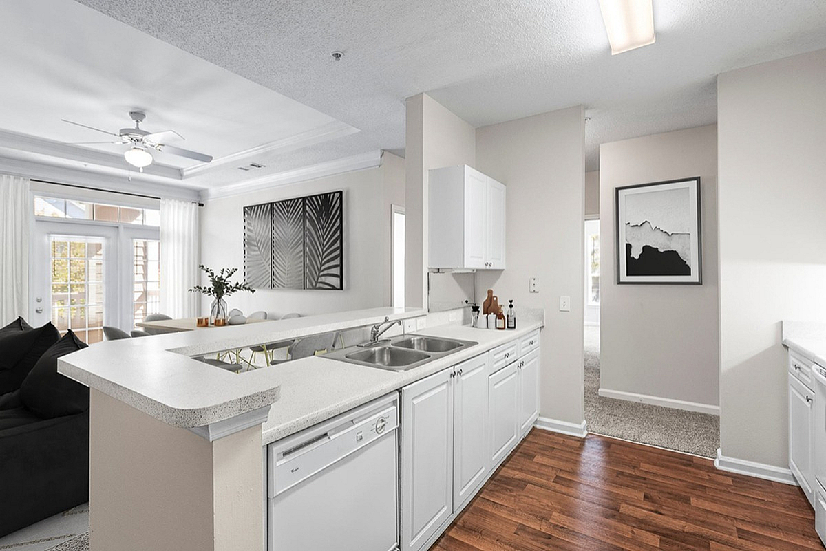 Elegant open-concept kitchen at Retreat at Peachtree City Apartments with modern white cabinets, wooden flooring, and a cozy living area perfect for gatherings.