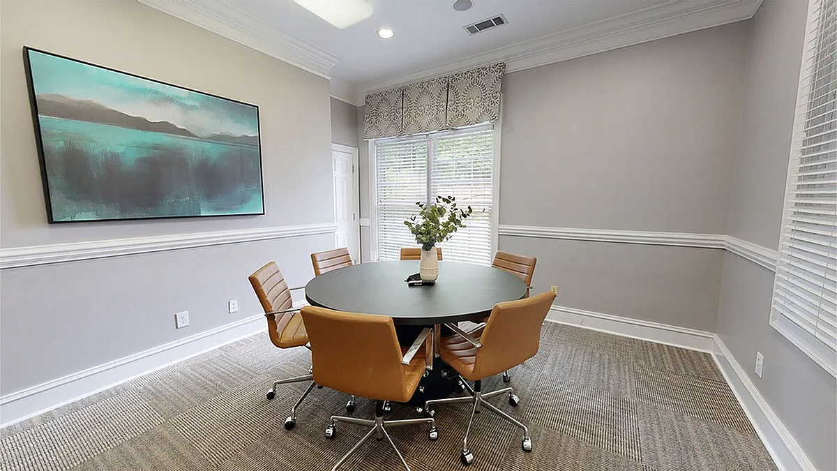 Elegant meeting room at Retreat at Peachtree City Apartments with sleek round table, leather chairs, and artistic wall decor.