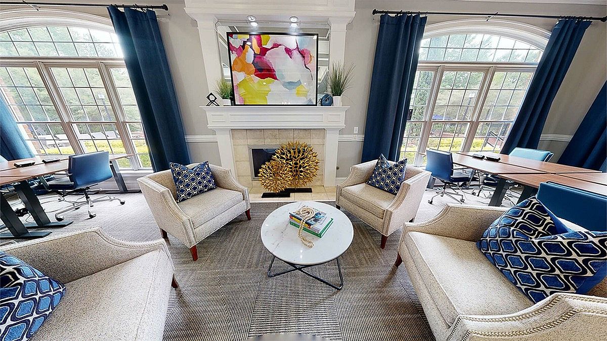 Chic and inviting lounge area at Retreat at Peachtree City Apartments with plush seating, vibrant artwork above a modern fireplace, and large windows allowing natural light to flood in.