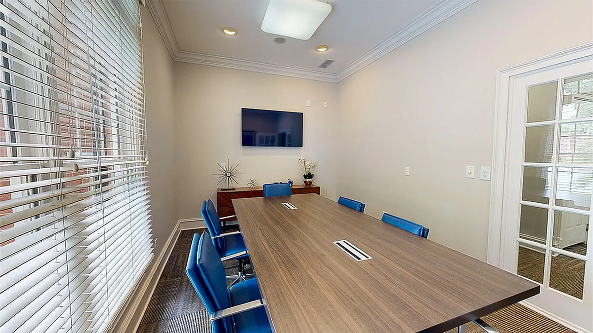 Elegant conference room at Retreat at Peachtree City Apartments with a modern wooden table, bright blue chairs, and a mounted flat-screen TV, perfect for meetings and collaborations.