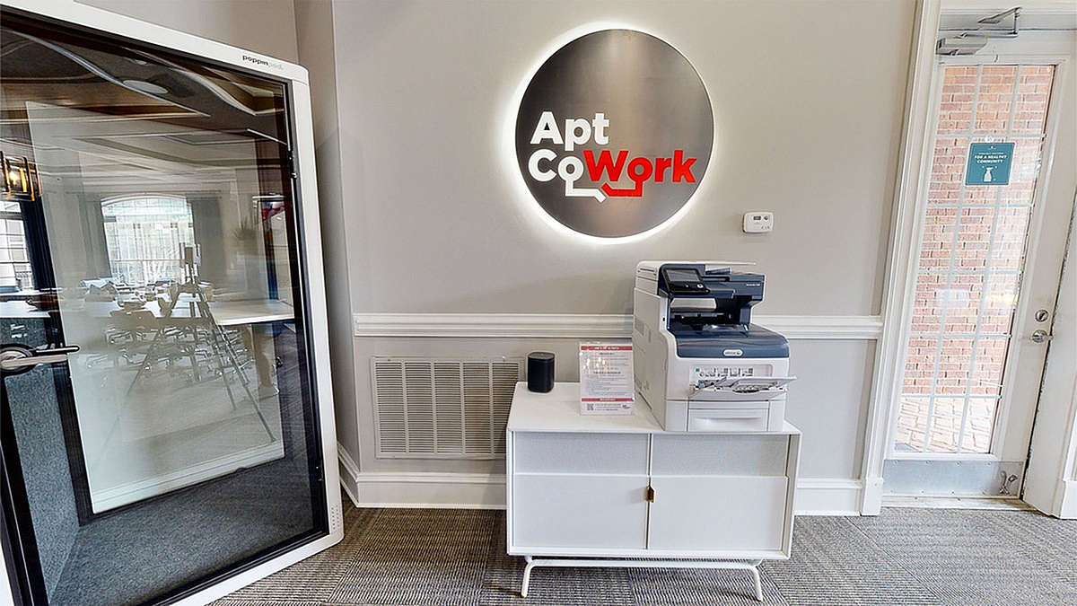 Modern coworking space at Retreat at Peachtree City Apartments entrance featuring sleek glass booth, stylish decor, and multifunction printer, ideal for productivity and collaboration.