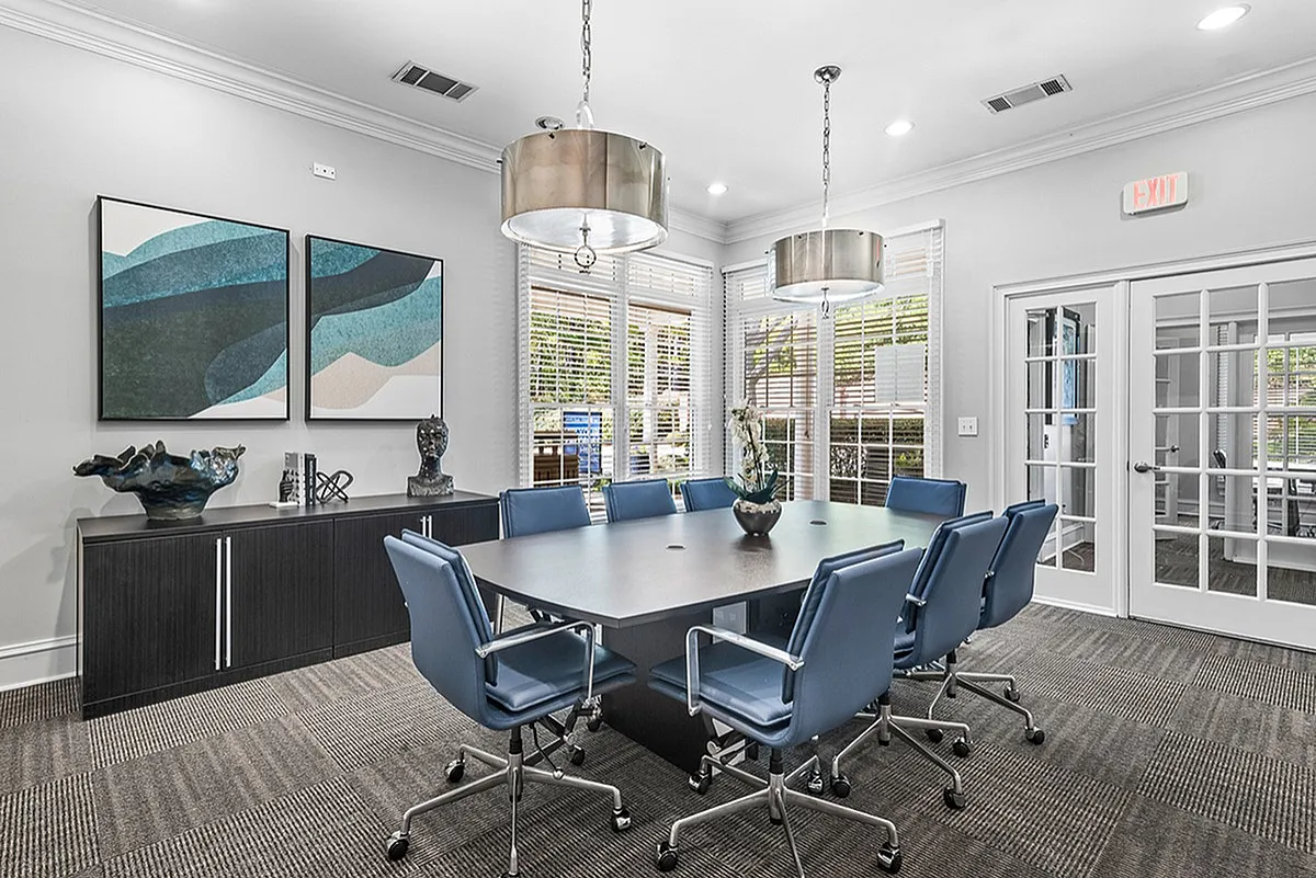 Modern conference room at Retreat at Peachtree City Apartments with sleek blue chairs around a polished table, stylish artwork, and abundant natural light.