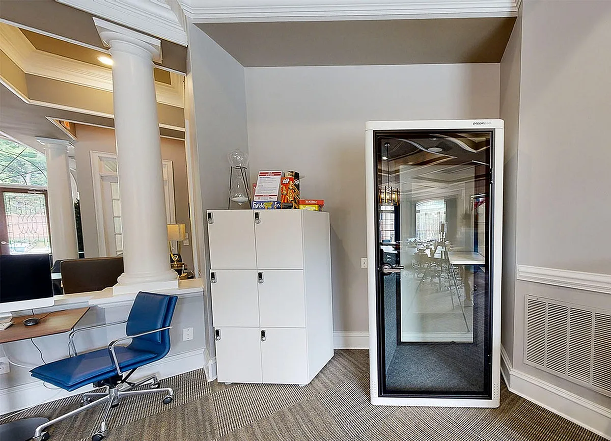 Modern office space at Retreat at Peachtree City Apartments showcasing a sleek workstation, stylish blue chair, and innovative soundproof pod for private calls.