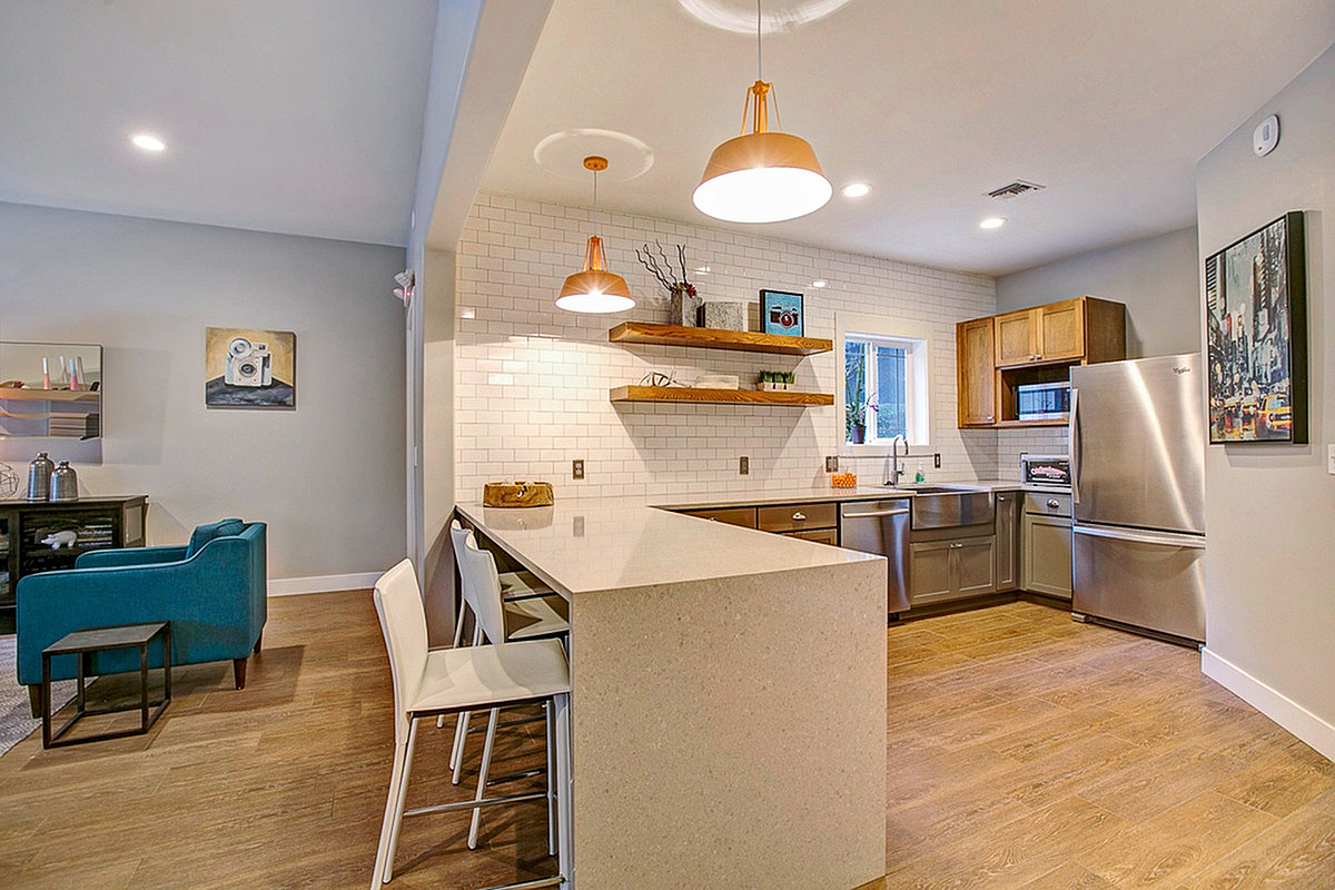 Modern clubroom kitchen with sleek white countertops, stainless steel appliances, and warm wooden accents adjacent to a cozy lounge area at Scott Mountain Apartments.