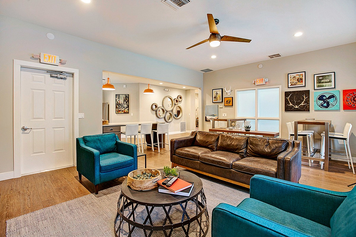 Inviting open-concept clubroom at Scott Mountain Apartments featuring a stylish brown leather sofa, vibrant teal armchairs, and modern art decor on the walls, perfect for relaxation and entertaining.