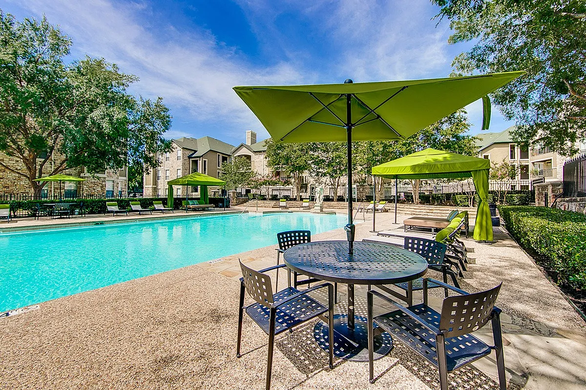 Luxe apartment community showcasing a pristine outdoor pool with elegant umbrellas and comfortable lounge chairs, surrounded by lush greenery at Stonebriar of Frisco Apartments.