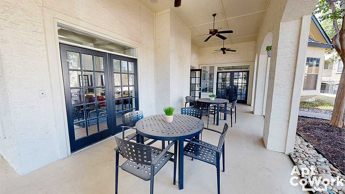 Charming outdoor patio at Stonebriar of Frisco Apartments with modern tables, stylish seating, and lush greenery, perfect for relaxation in a vibrant apartment complex.