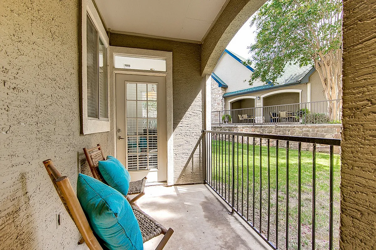 Charming apartment patio at Stonebriar of Frisco with cozy seating, offering a serene view of lush green garden and elegant stone architecture.