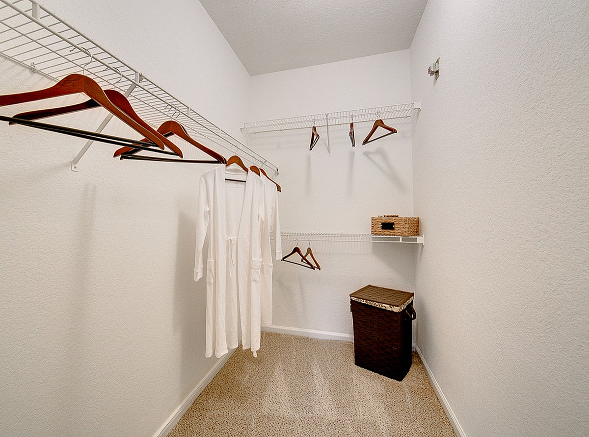 Spacious walk-in closet at Stonebriar of Frisco Apartments with sleek white walls, modern wire shelving, and stylish wooden hangers for a luxurious living experience.