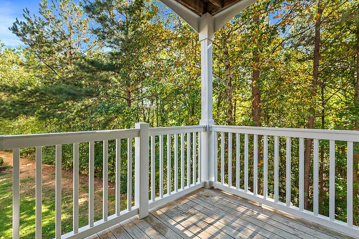 Inviting wooden balcony with white railing overlooking lush green trees, offering serene outdoor relaxation at Summer Park Apartments in Buford, GA.