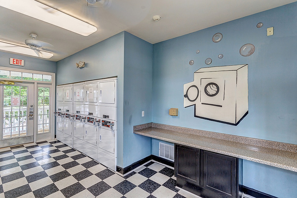 Bright and modern laundry room at Summer Park Apartments with vibrant blue walls, playful washer art, black and white checkered floor, and convenient counter space.