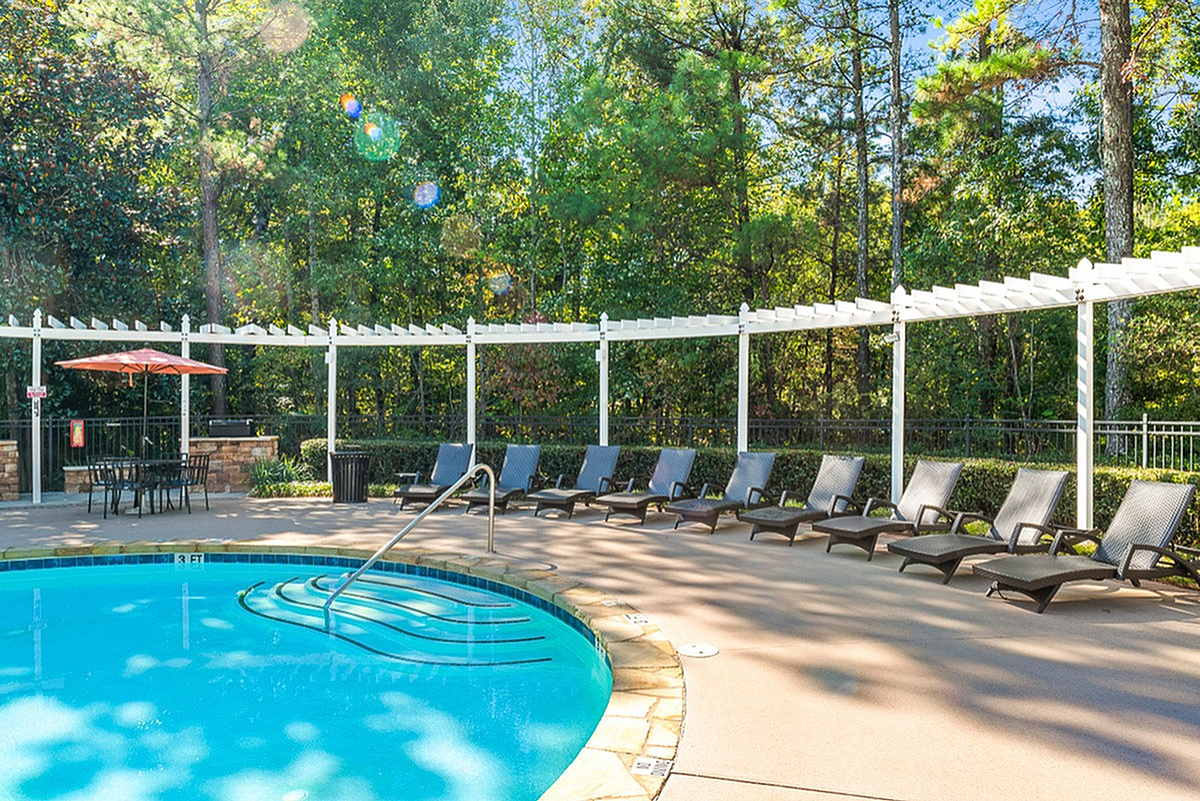 Inviting outdoor pool at Summer Park Apartments with sun loungers and pergola, surrounded by lush greenery, perfect for relaxation and leisure.