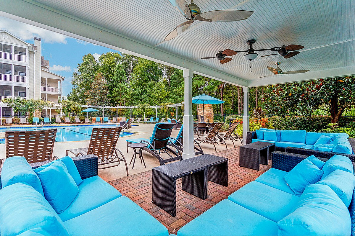 Summer Park's luxurious poolside area featuring a covered lounge with plush blue seating, surrounded by lush greenery and modern amenities.